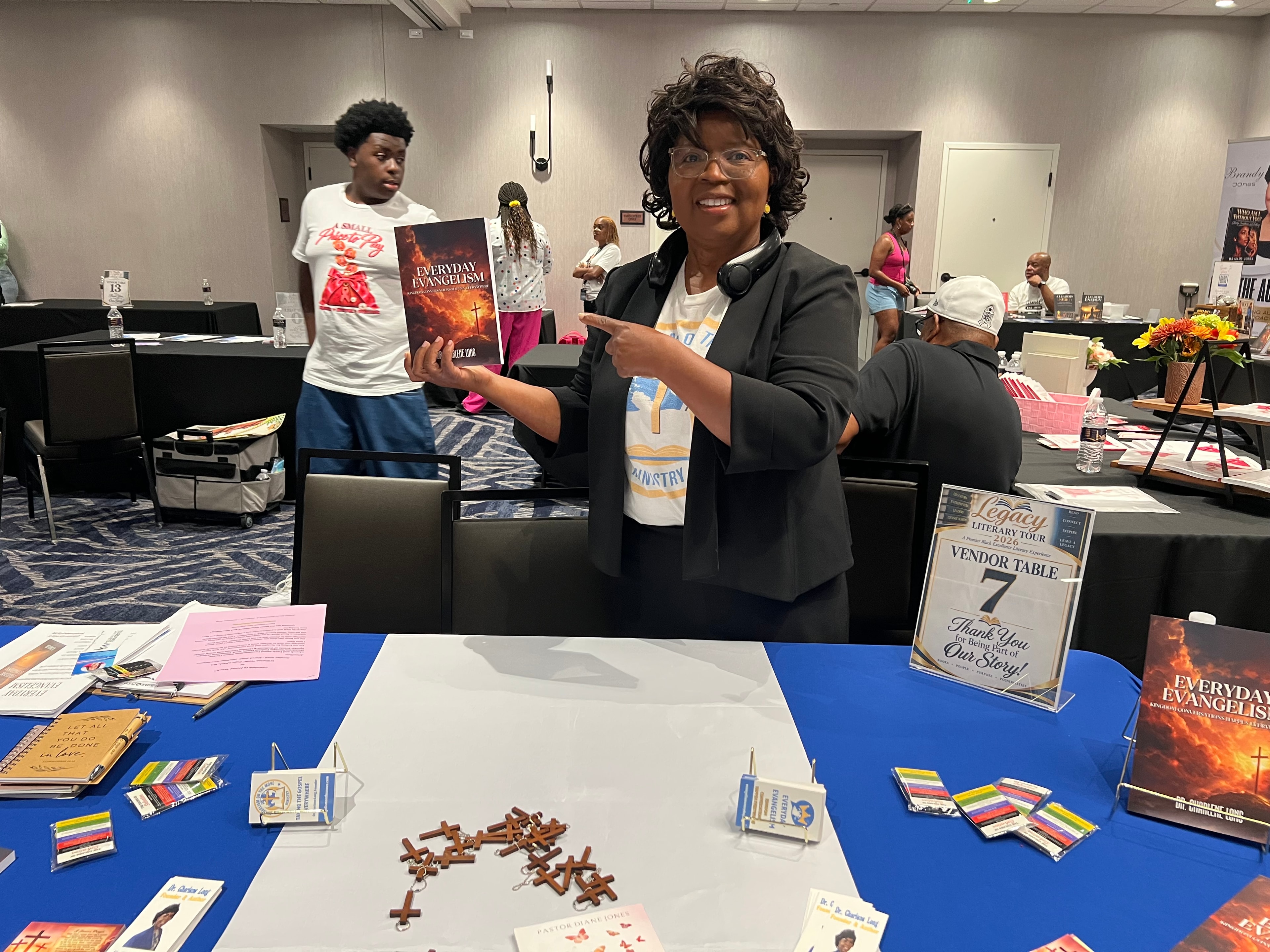 Dr. Charlene Long pointing to Everyday Evangelism at her vendor table — Legacy Literary Tour 2026
